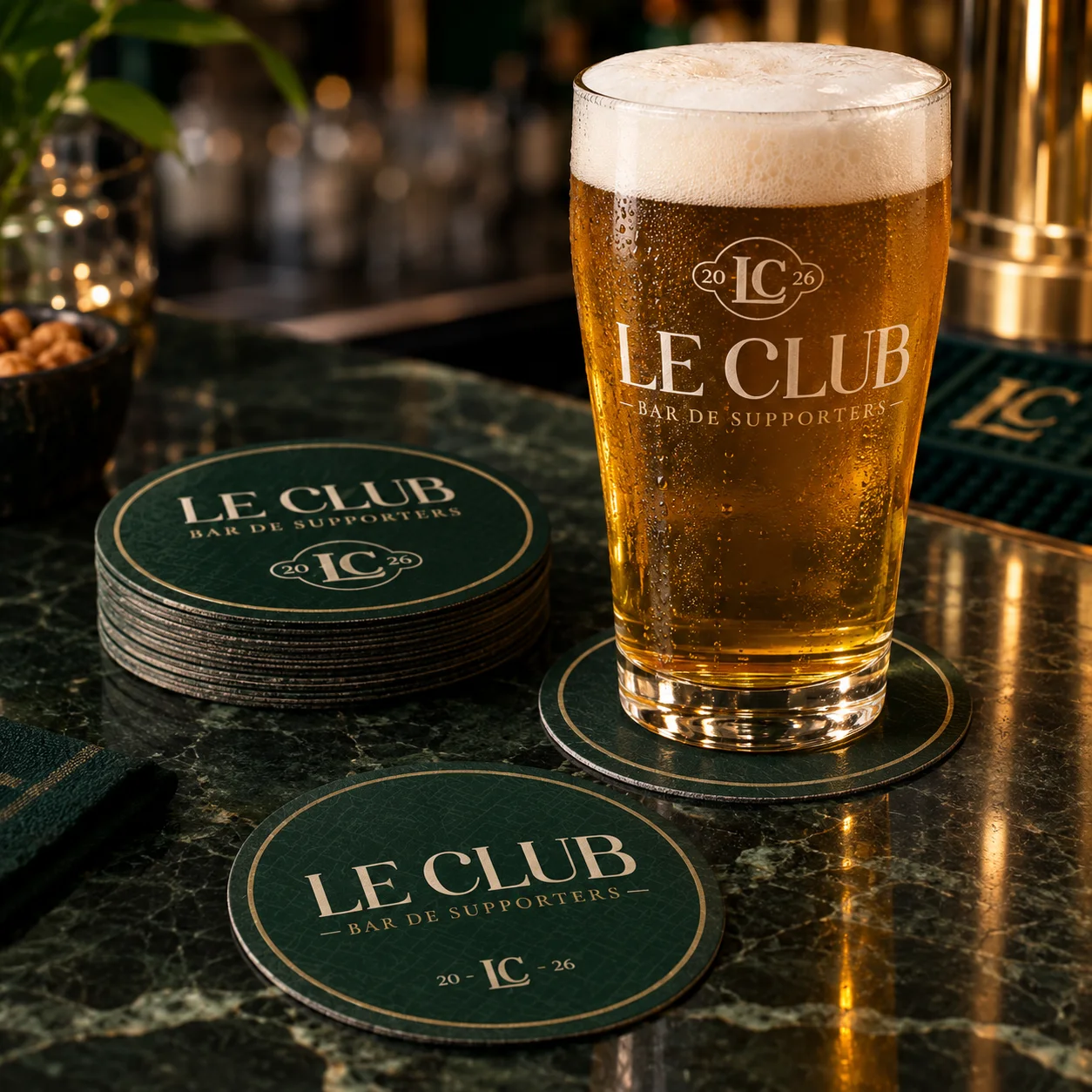 Pinte de bière dorée floquée Le Club posée sur un sous-bock vert, comptoir en marbre