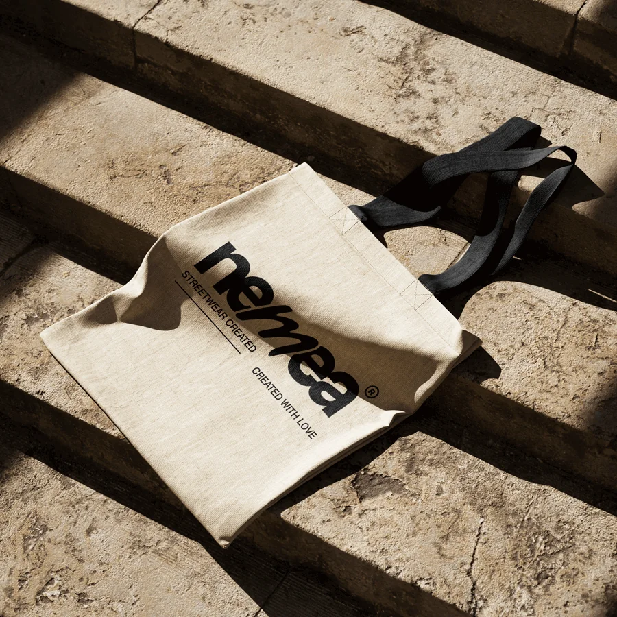 Tote bag Nemea écru avec logotype noir, posé sur des marches en pierre