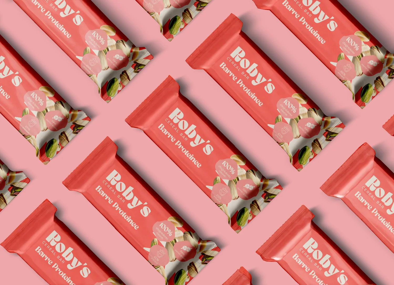 Emballages individuels rouges de la barre protéinée Roby's, disposés en motif sur fond rose